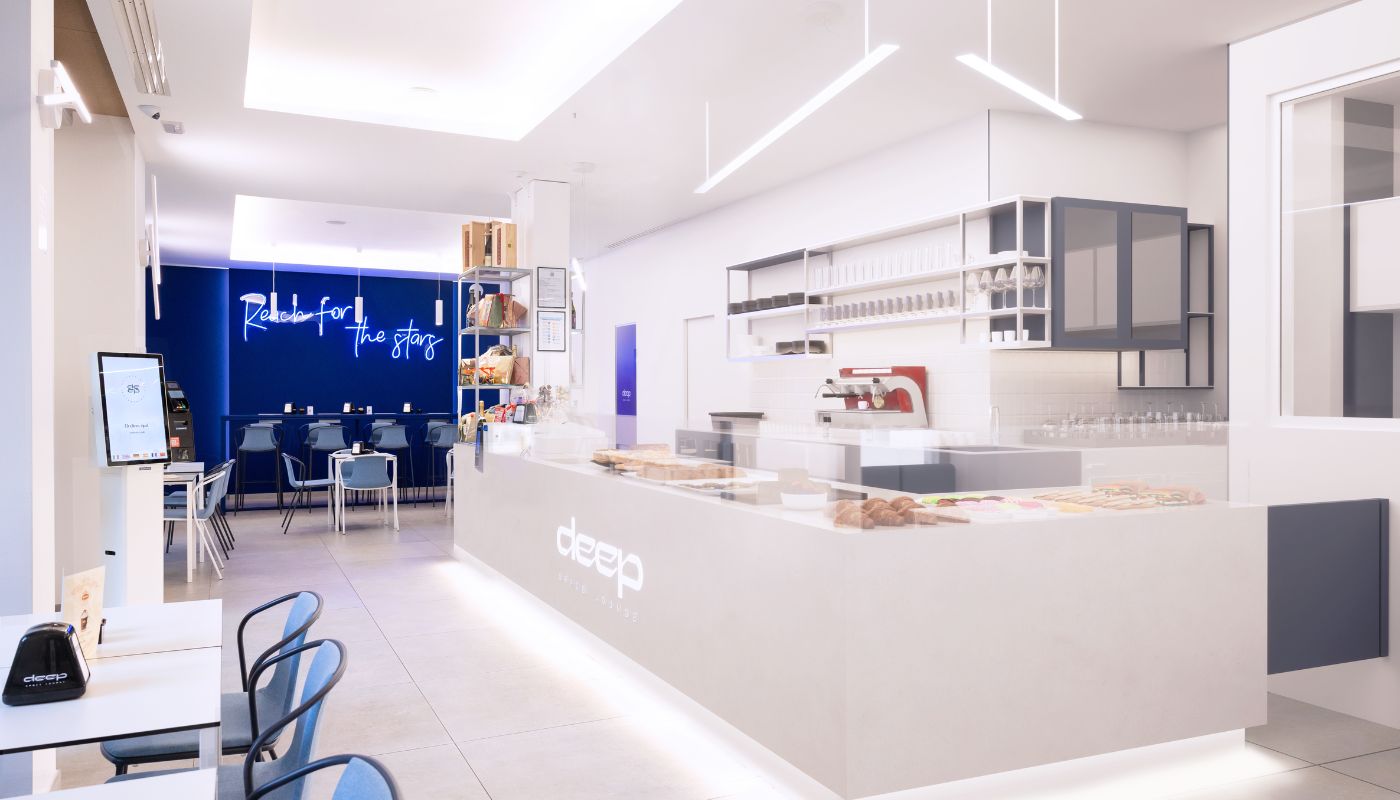 Interno di Deep Space Lounge con banco luminoso e parete blu con insegna al neon.